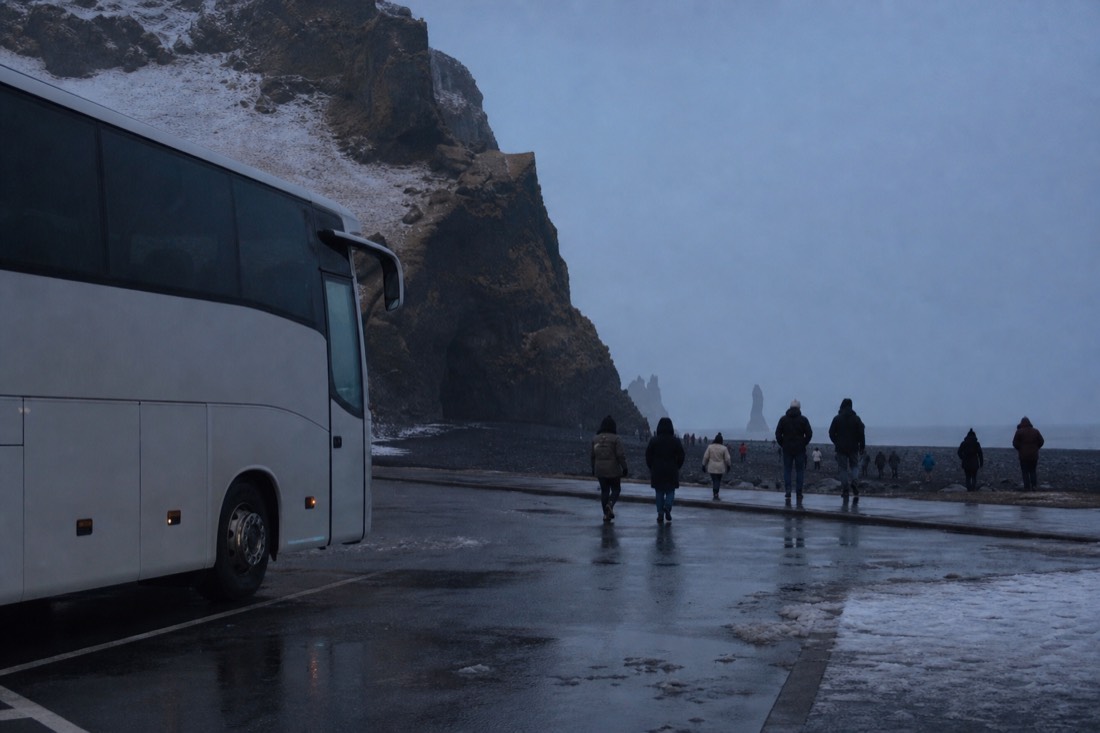 Tour coach parked in the Reynisfjara car park at dusk, small figures returning across black sand