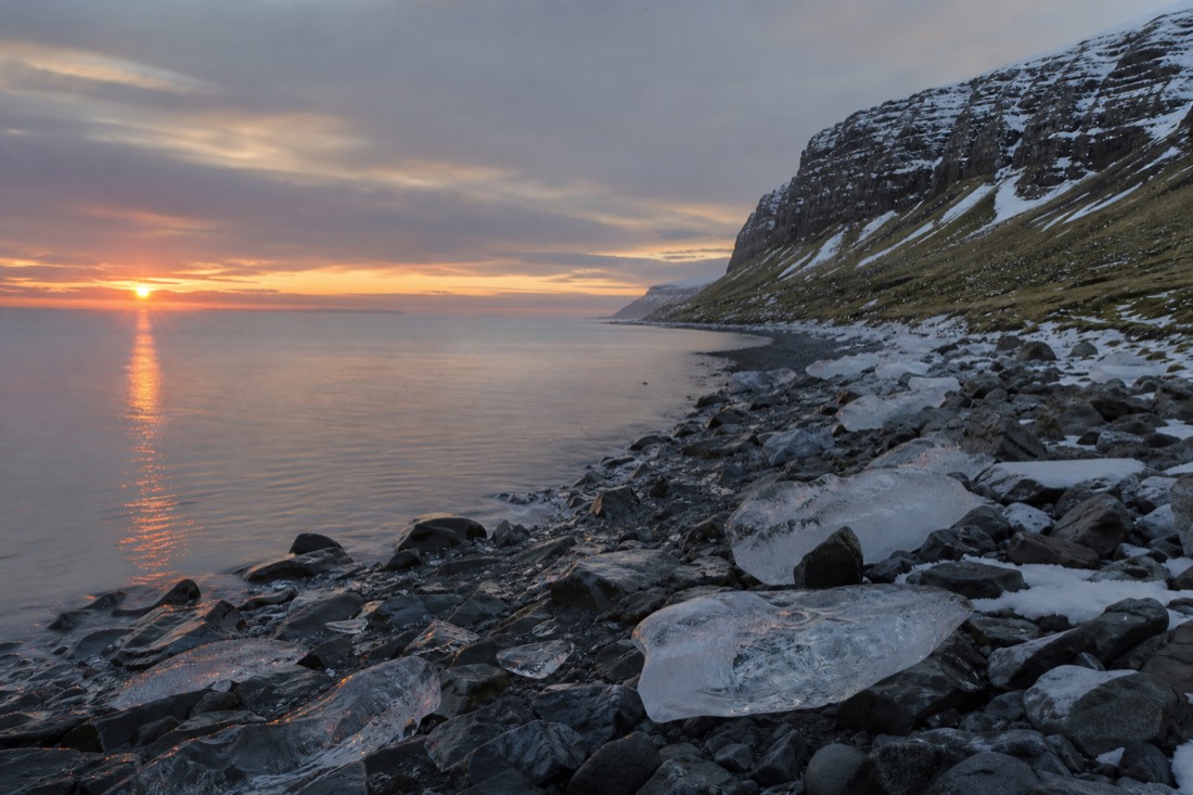 Midnight sun low over a green Icelandic coastline, calm sea, nobody in the frame