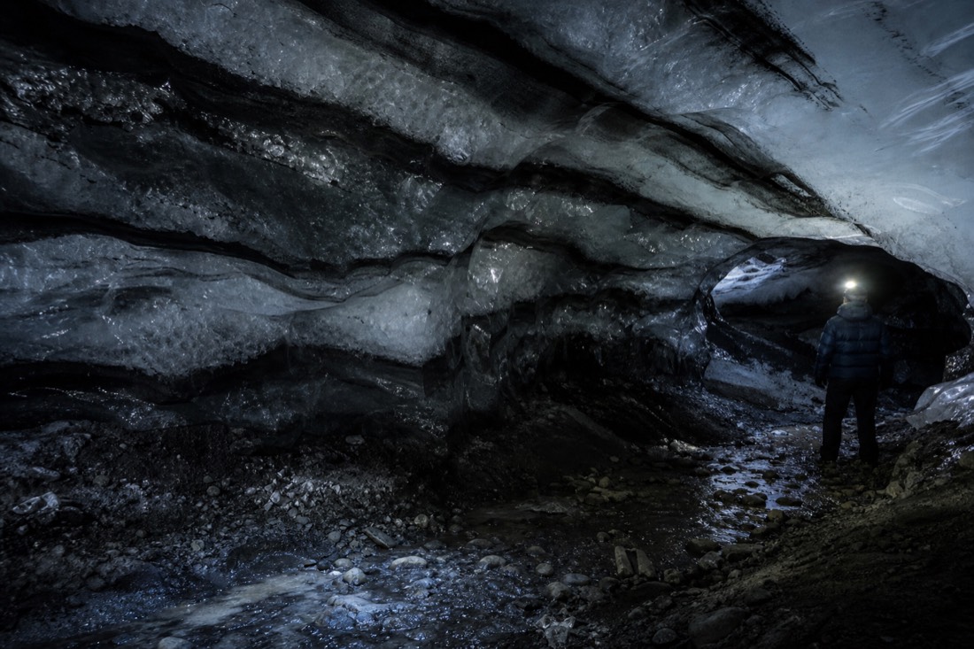 Dark ash-banded ice wall inside a Katla cave lit by a single headtorch beam