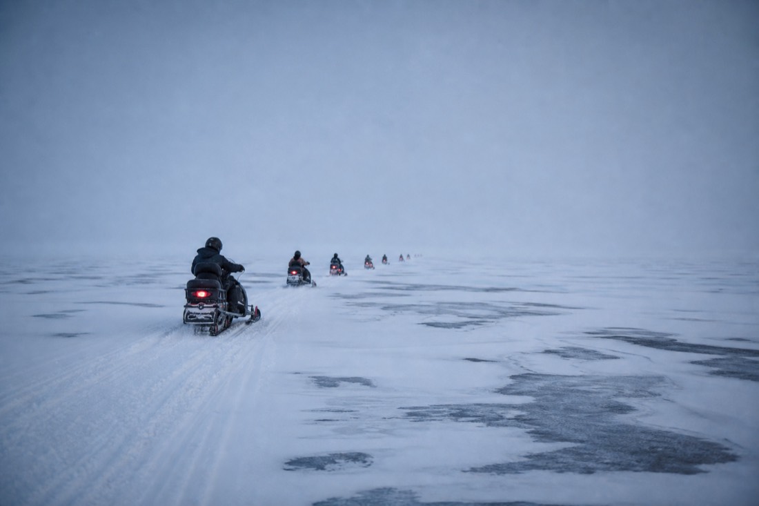 Single file of distant snowmobiles crossing flat white Langjokull ice under grey overcast, no horizon