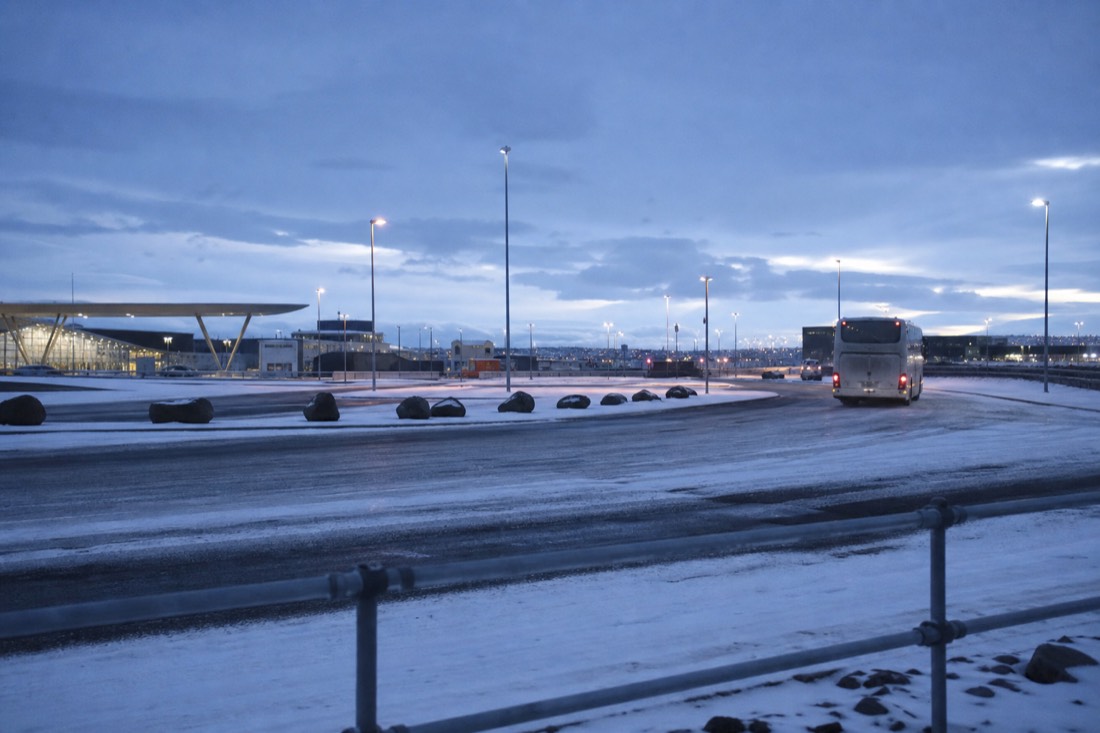 Empty Reykjavik pickup bay at first light, one coach pulling away, fresh snow on the tarmac