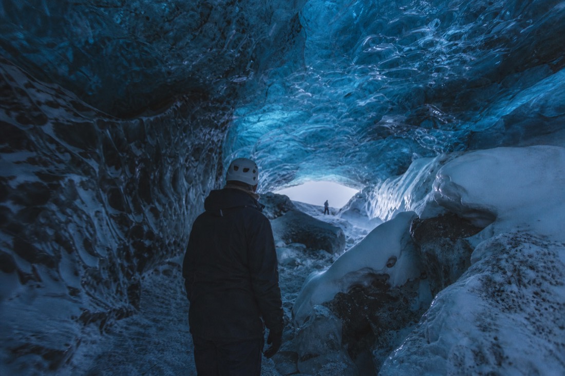 A guide in a helmet inside a blue natural ice cave under the Vatnajökull glacier