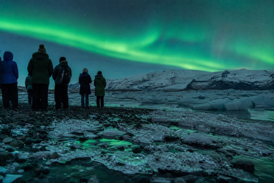 A small group photographed under the aurora on a northern lights photo tour in Iceland