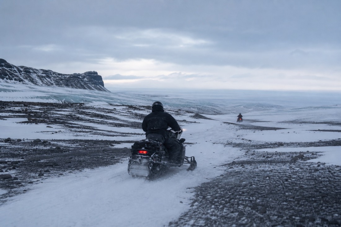Riders in snowsuits and helmets on Langjökull glacier during a winter snowmobile tour