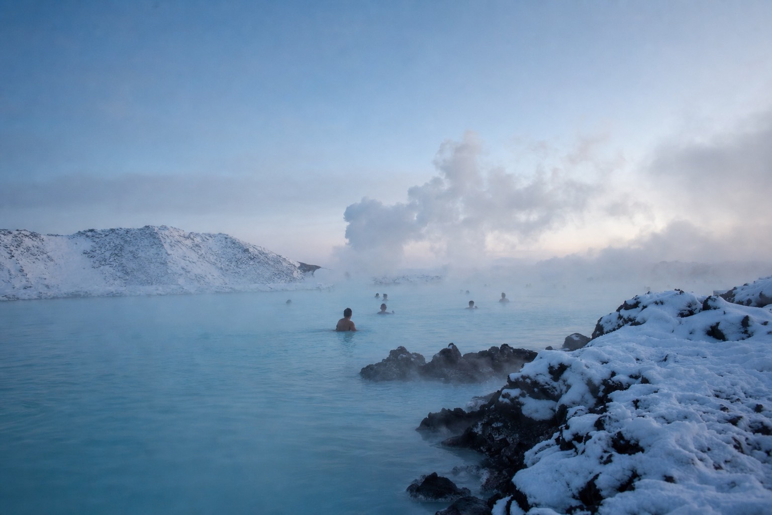 Steam drifting over the milky blue water of a geothermal lagoon in the Icelandic snow