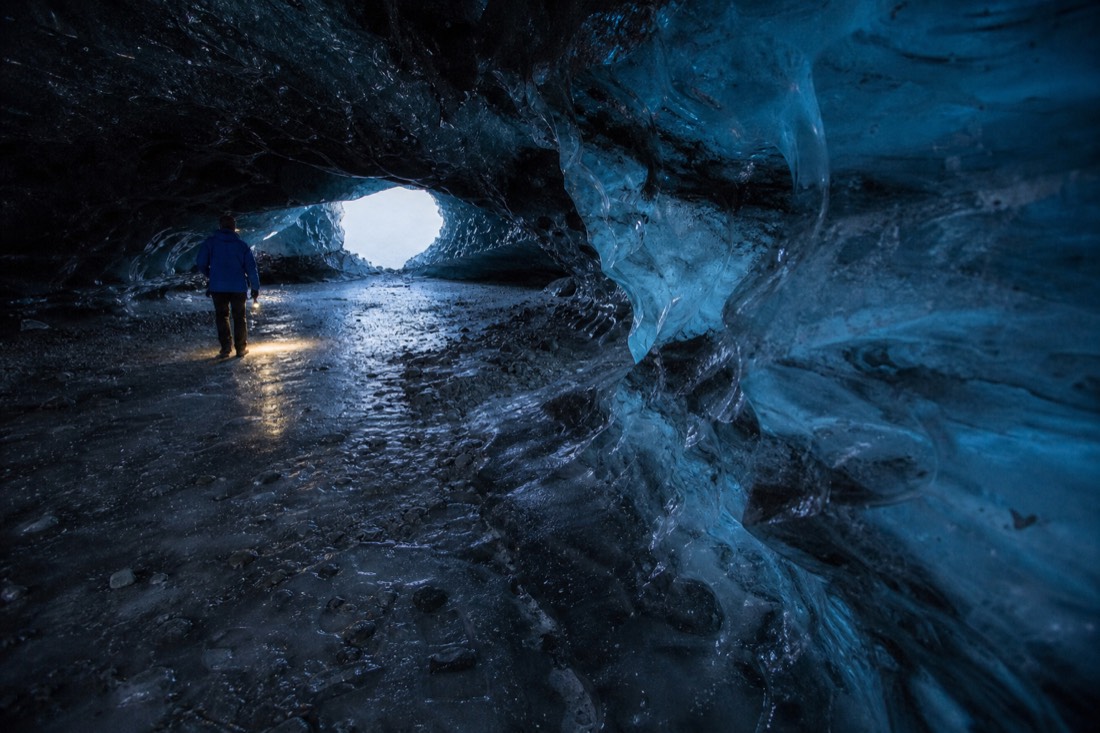 Torchlight on wet blue ice inside a natural cave under Vatnajokull, ash bands visible