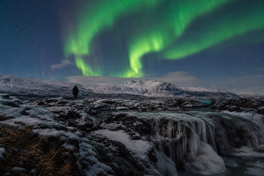 Bright green aurora curtain overhead on a clear cold night above snow-covered lava