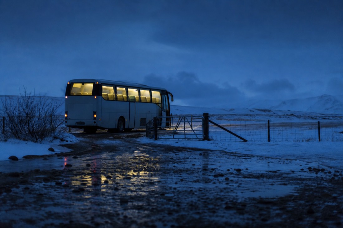 Tour coach parked on a snowy farm track at night, interior lights glowing under a dark sky