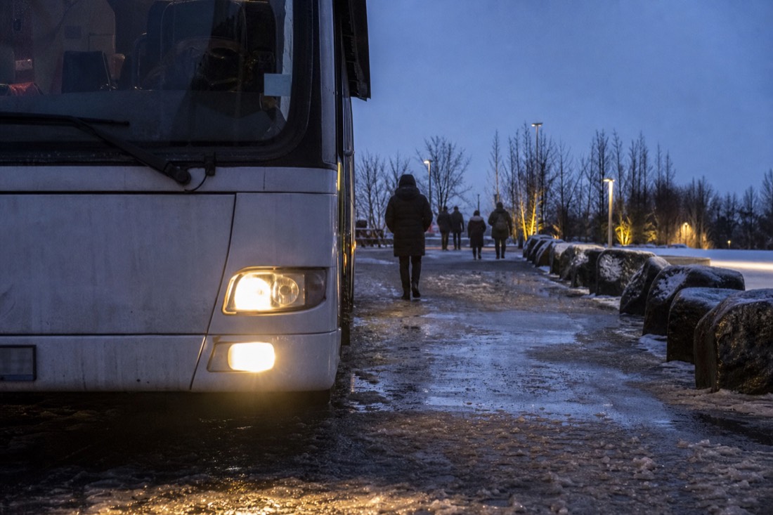 Coach headlights idling at a snowy Reykjavik pickup stop in full dark, slush on the pavement