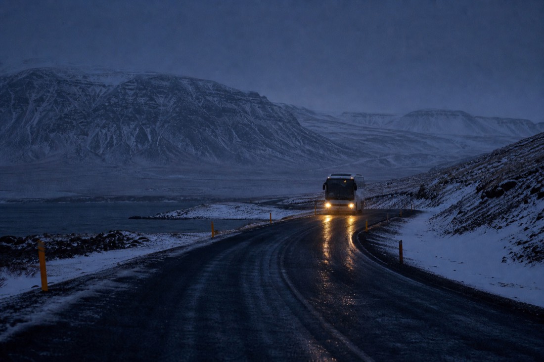 Coach headlights on a dark December road east of Reykjavik, snow banks either side