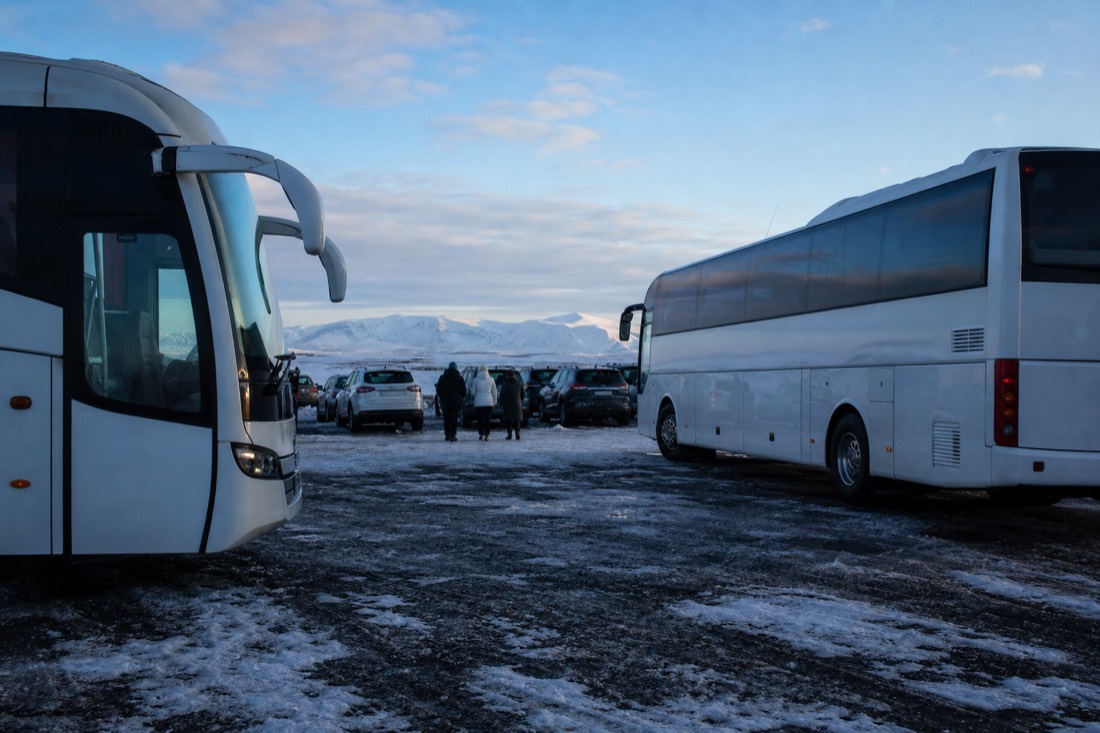 Coaches parked in a busy February car park at Thingvellir, snow underfoot and bright sky