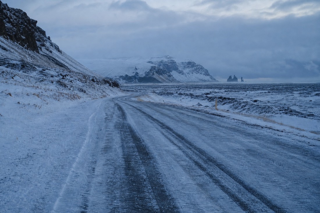 Studded tyre tracks on a frozen January road east of Vik under flat grey light