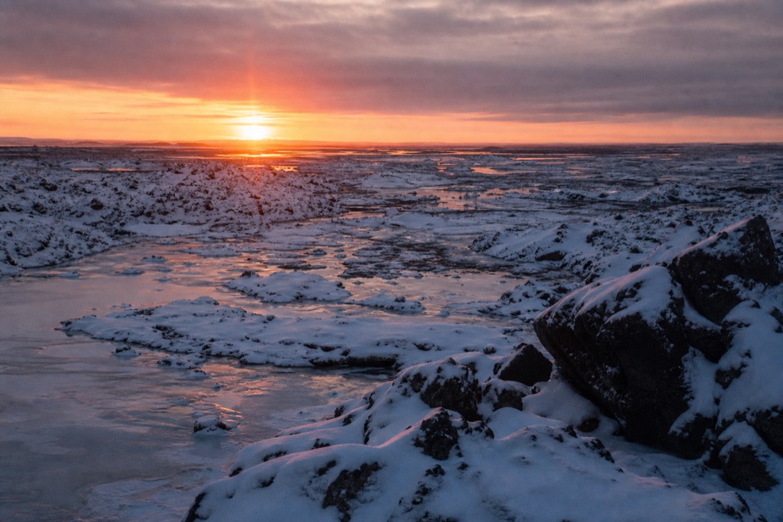 Low orange midday sun barely clearing the horizon over snow-covered lava fields near Reykjavik