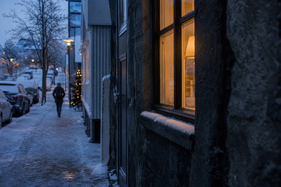 Snow-covered Reykjavik side street at dusk, warm light spilling from a window onto the pavement