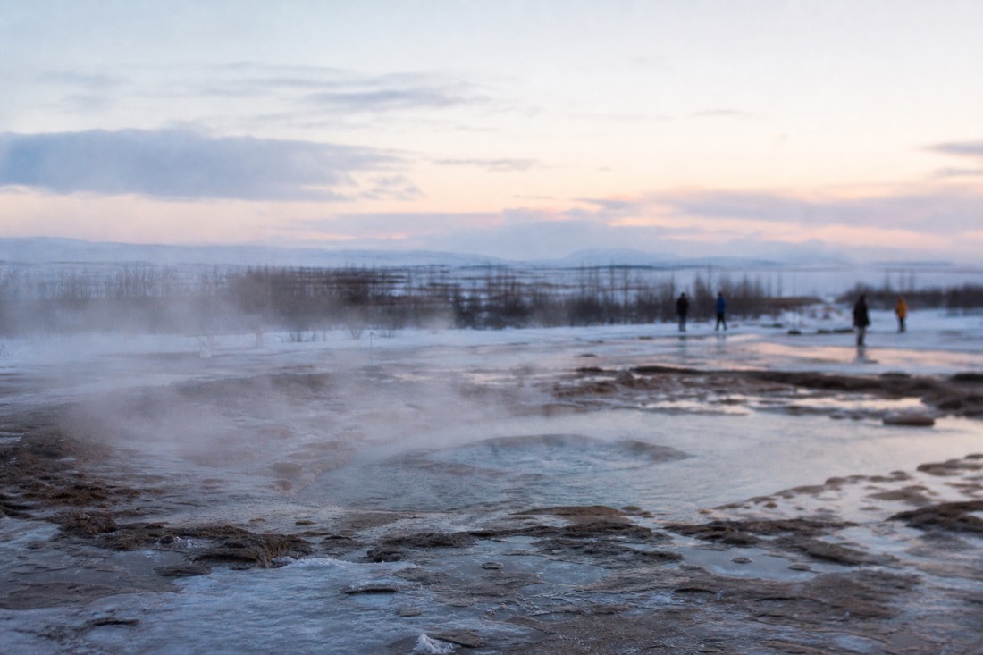 Steam hanging over Strokkur in still freezing air, snow lying beside the bare warm ground