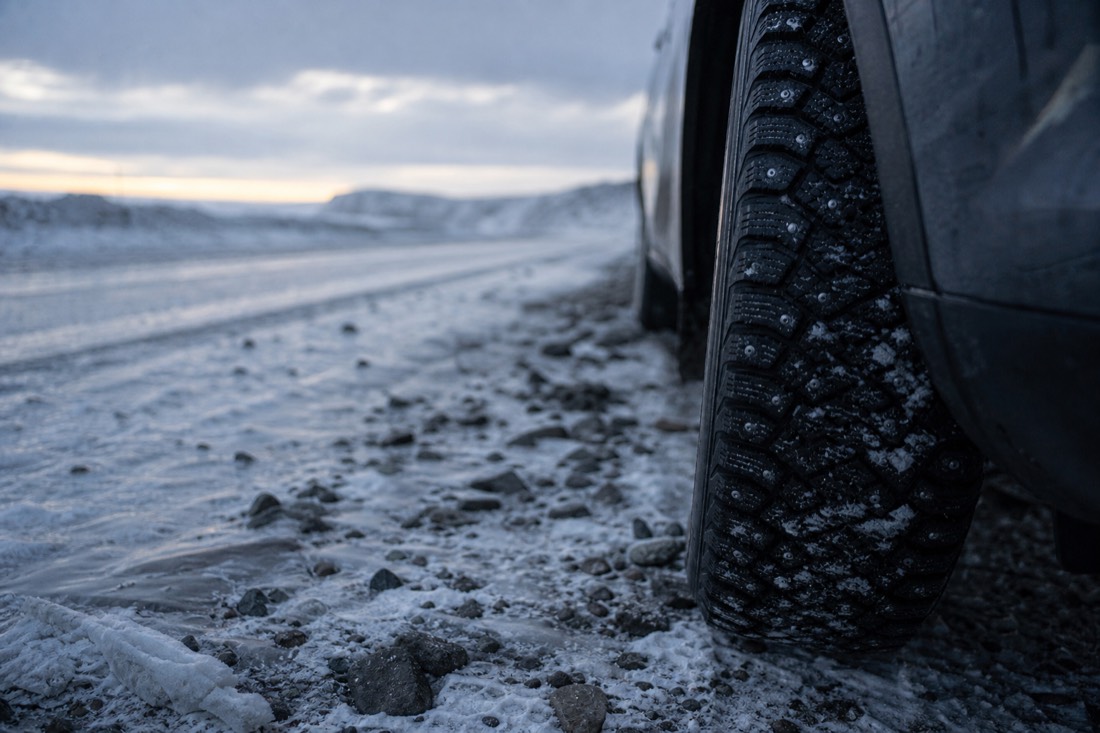 Studded winter tyre on packed snow at the edge of a gritted Icelandic road, close crop