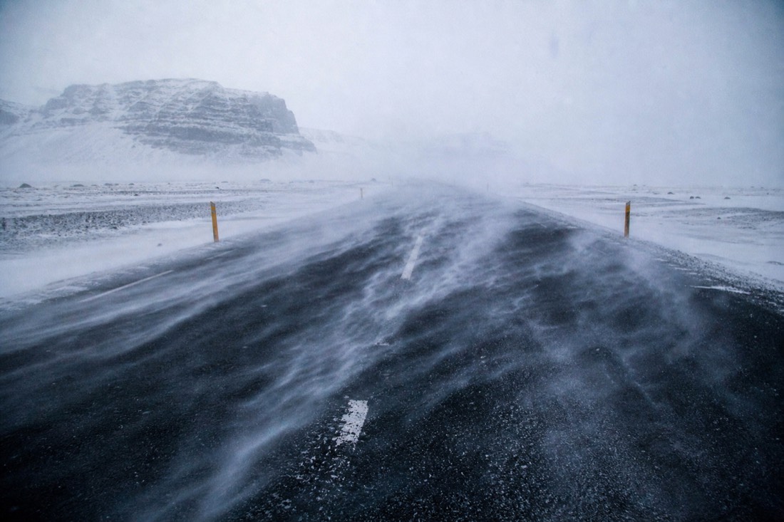 Loose snow streaming sideways across an exposed Icelandic road in strong wind, poor visibility