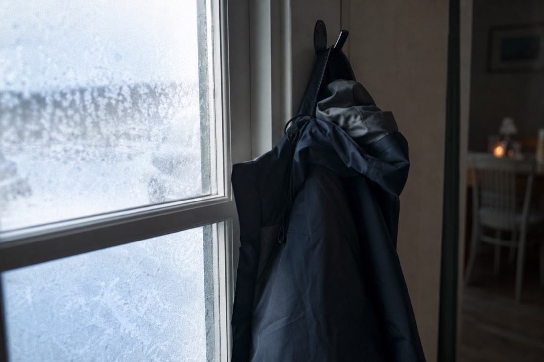 Windproof hardshell jacket hanging on a hook by a frosted window in flat interior daylight