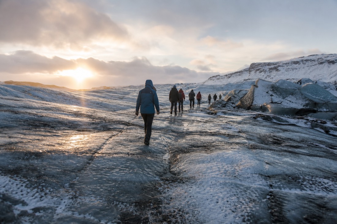 Distant walkers in waterproof shells crossing hard glacier ice under low arctic sun