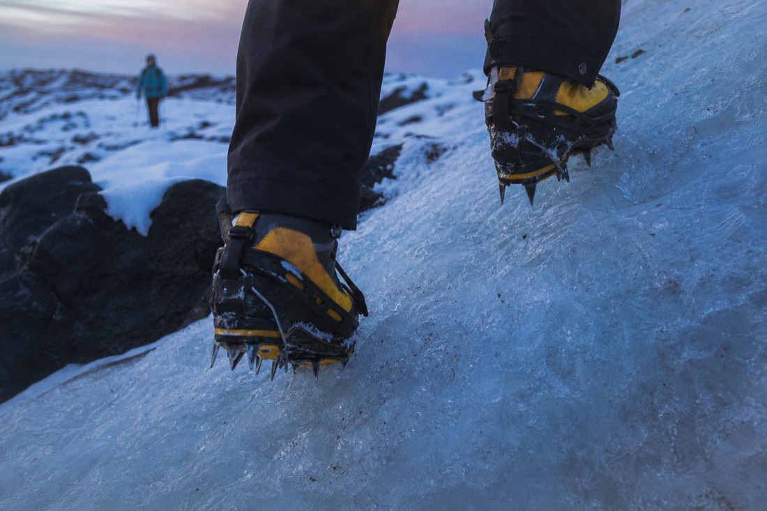 Crampon points biting into hard glacier ice on an uneven approach, close crop, no faces